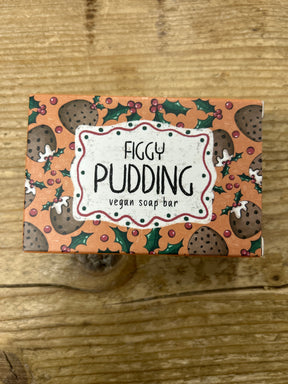 A box of Figgy Pudding Vegan Soap Bar, featuring figgy pudding, holly leaves, and berries artwork on a wooden background.