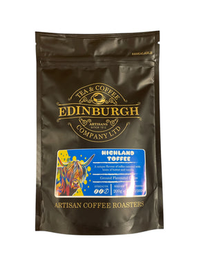 A black resealable 200g bag of Highland Toffee Ground Coffee by Edinburgh Tea & Coffee Co., featuring a colorful highland cow and gold text, captures Scottish artisan coffee style on the packaging.