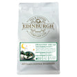 A 200g white bag of Dragons Decaf from Edinburgh Tea & Coffee Company, adorned with a dragon illustration and a label emphasizing the Swiss Water decaffeination process. This decaf coffee features subtle caramel and peanut notes, with a best before date of 07/01/2027.