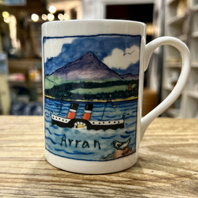 The Elspeth Gardner Waverley Arran Mug features a ferry on blue water with mountains and trees, plus "Arran" below the scene. This charming ceramic mug adds a playful touch to any space.