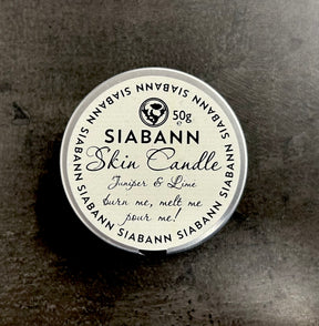 A 50g Siabann Juniper & Lime Skin Candle rests on a dark surface. Its label reads, "burn me, melt me, pour me!"—showing it doubles as a nourishing massage oil for your skin.