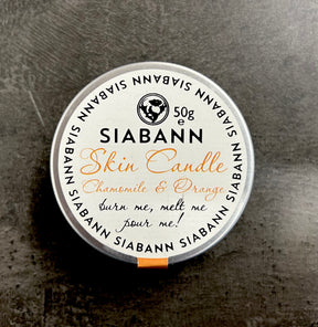A 50g round tin labeled "Siabann Chamomile and Orange Candle" features chamomile and orange scent, natural oils, decorative text on a dark background, and the phrase "burn me, melt me, pour me!" on the label.