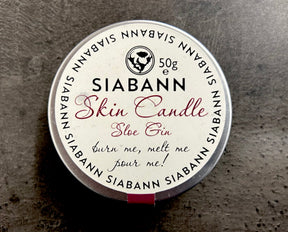 The Siabann Sloe Gin Skin Candle 50 g, labeled "burn me, melt me, pour me!", sits on a gray textured surface—this candle melts into a luxurious massage oil made from natural oils.