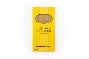 A yellow box labeled "James Chocolates Luxury Bar of Caramel Chocolate" displays visible caramel chocolate pieces through a clear window. The packaging indicates a weight of 100 grams, resembling an enticing caramel chocolate bar, elegantly placed on a dark surface.