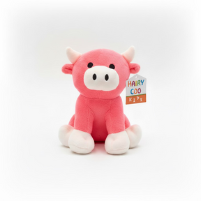 The Hairy Coo Kids Plush Toy is a pink plush cow with white horns, feet, and snout, black eyes, and a colorful "Hairy Coo Kids" tag. It sits upright against a plain white background.