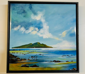 Holy Isle from Lamlash Ceramic Tile features a calm seascape with scattered rocks in the foreground, green hills on a distant island, and a blue sky with white clouds. Tile size: 12 x 8.5 inches.