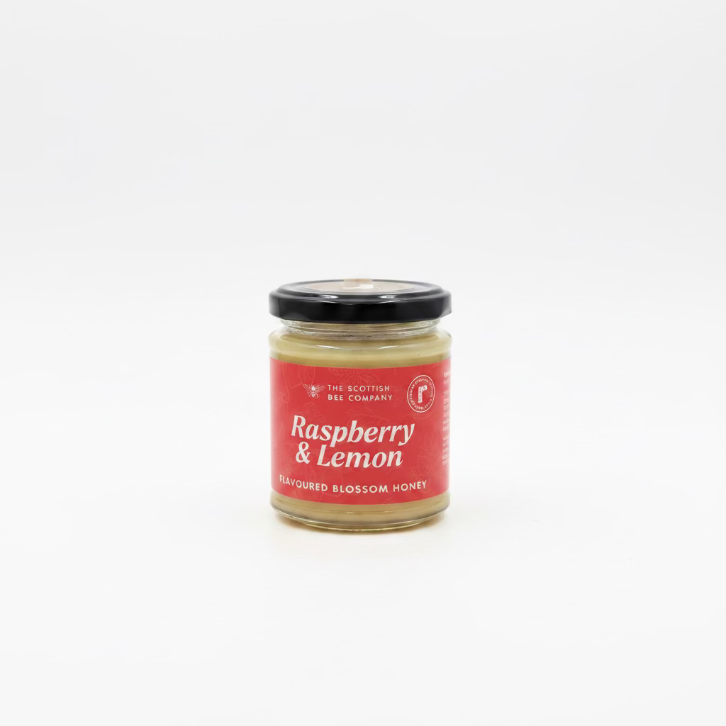A jar of Raspberry & Lemon Flavoured Blossom Honey from The Scottish Bee Company The product is in a clear glass jar with a black lid and a red label featuring white text.