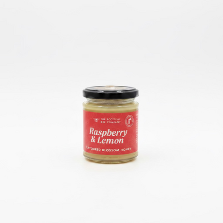 A jar of Raspberry & Lemon Flavoured Blossom Honey from The Scottish Bee Company The product is in a clear glass jar with a black lid and a red label featuring white text.
