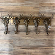 The Brass Buffalo Hooks is a wall-mounted rack featuring five metal hooks shaped like steer skulls, displayed against a wooden floor.
