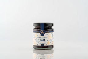 A glass jar of Winter Fruits Jam with a white label featuring gold snowflake illustrations and text that reads “Winter Fruits Jam with Cinnamon.”