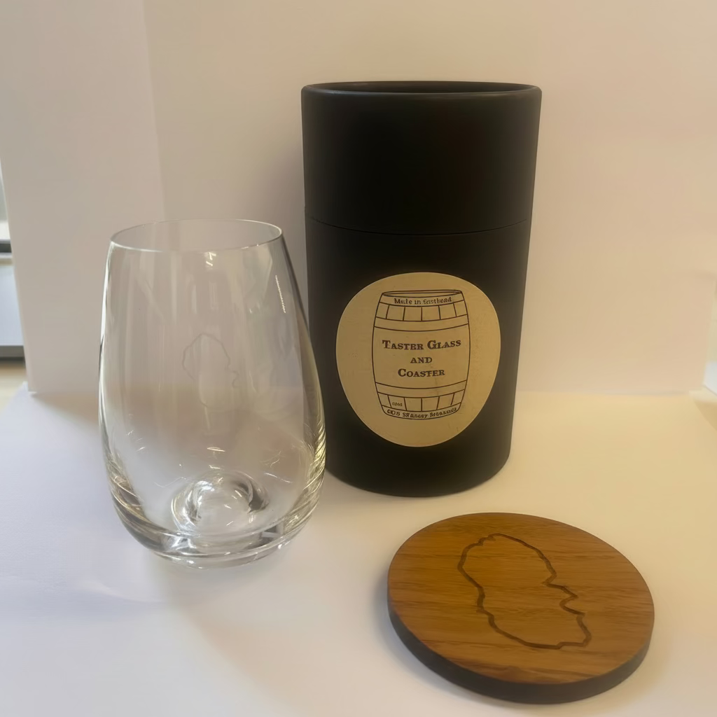 The Arran Whisky Shot Glass & Coaster Gift Set includes a clear whisky shot glass, a black cylindrical container, and a round wooden coaster with matching logos—a perfect Scotland souvenir displayed on a white background.