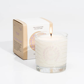 A lit Isle of Skye Chamomile and Cedar Tumbler Candle made with natural soya wax rests in a clear glass jar with its labeled box, both set against a plain white background.
