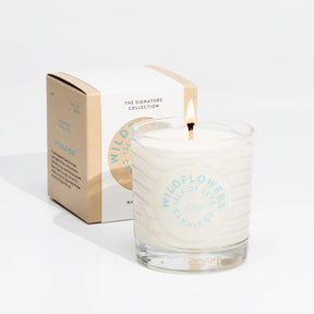 A lit Isle of Skye Wildflowers Tumbler Candle in a glass jar sits before its matching box, filling the space with a handmade floral scent against a plain white background.