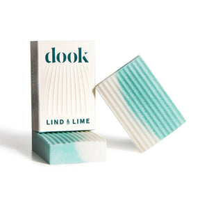 Two rectangular bars of light blue and white marbled Dook x Lind & Lime Salt Soap with ridged surfaces are shown by a white "dook" and "LIND & LIME" box. This artisanal soap is inspired by Lind & Lime Gin and truly handcrafted.