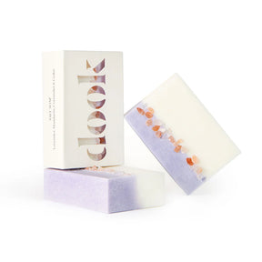 Three artisanal bars of white and lavender salt soap, topped with pink salt crystals, are packaged in white with "dook" prominently displayed. The soaps feature a blend of Lavender, Mandarin, Coriander, & Cedar.