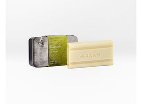 A rectangular beige Machrie Soap 200g bar with "ARRAN" embossed, placed next to a metal tin with a green "MACHRIE ARRAN soap bar" label, on a plain white background.