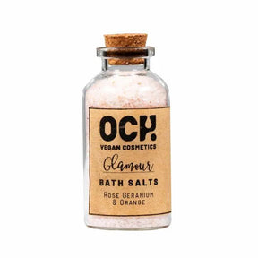 A small glass jar with a cork lid labeled "Rose Geranium Bath Salts," filled with pinkish Himalayan salt crystals—ideal for relaxing self-care routines.