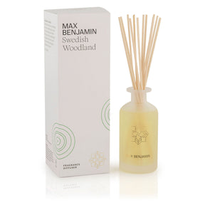 The Max Benjamin – Swedish Woodland Reed Diffuser, hand-crafted in Ireland with natural essential oils, includes a frosted glass bottle with pale liquid and reed sticks, displayed next to a white box decorated with green tree rings.