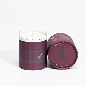 Two plaid-patterned soya wax candles in dark red holders; one stands upright while the other lies on its side, revealing a lid that displays a map of Scotland and the text “Handmade in the Highlands of Scotland”—an inviting nod to the Isle of Skye Heather and Wild Berries Large Candle, handmade on the Isle of Skye.