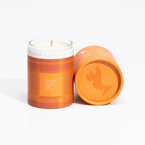 The Isle of Skye Island Whisky Miniature Candle is a handmade soya wax candle in an orange plaid container, shown upright beside its matching cylindrical lid, which displays a white geographic outline and text in a minimalist style.