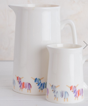 A small white ceramic jug called "Hairy Coo Small Jug", featuring colorful abstract animal designs—possibly donkeys or llamas—along the bottom edge, set against a soft, light background.
