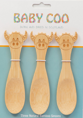 Three Baby Coo - Highland Cow Bamboo Spoons with adorable engraved cow faces are displayed on blue and white packaging labeled "BABY COO Born and Bred in Scotland." Text below: "Three Natural Bamboo Spoons.
