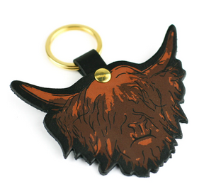 The Clare Baird Highland Cow Keyring features a brown, cartoon-style highland cow head with long horns and shaggy fur, crafted from sturdy genuine leather and finished with a gold ring. Proudly made in Scotland, this charming accessory adds a playful touch to any set of keys.