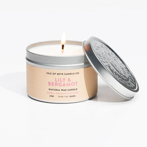 A lit Lily & Bergamot Travel Tin by Isle of Skye Candle Company sits with its lid askew; the label highlights a floral, delicate, and refined scent.