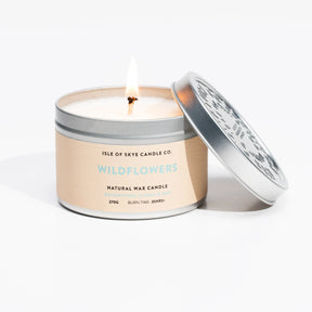 A lit Wildflower Travel Tin – Isle of Skye Candle Company candle sits in a round metal tin, lid to the side. The label features natural wax and a 35+ hour burn time.