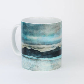 The Skye from Bealach Na Ba Applecross Mug is a white ceramic mug with a soft watercolor landscape of dark mountains, a blue lake, and a cloudy sky—an exclusive gift-ready design for nature lovers.