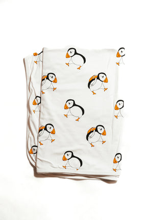 The Puffin Baby XL Blanket, handmade from organic cotton, showcases a white background with a playful pattern of black, orange, and white cartoon puffins.