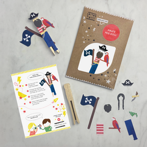 Make Your Own Pirate Peg Doll: This eco-friendly craft kit includes instructions, a wooden peg, stickers, and paper accessories—such as a flag, parrot, hat, and pirate costume pieces—displayed on a marble surface. It’s perfect for developing fine motor skills while creating your own adventurous pirate character!.