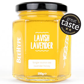 A glass jar of BeeHype Lavish Lavender Raw Honey, made by ethical beekeepers, features a black lid and a label with white text, a lavender illustration, and a "Great Taste 2020" two-star award badge in the top right corner.