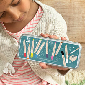 A child holds the Bright Mix Jumbo Watercolour Pencils Tin, featuring 10 jumbo watercolour pencils in a decorative tin adorned with colorful pencil illustrations and a pencil sharpener graphic, set against a light wooden background—an ideal mess-free alternative to paint and perfect for party favours.