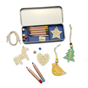 The Folk Art Christmas Decoration Kit includes a tin box filled with colored pencils, a sharpener, twine, wooden beads, and delightful folk art ornaments in the shapes of a horse, heart, star, tree, and bird—some of which are partially colored—making it the ideal plastic-free craft kit for creating beautiful Christmas decorations.