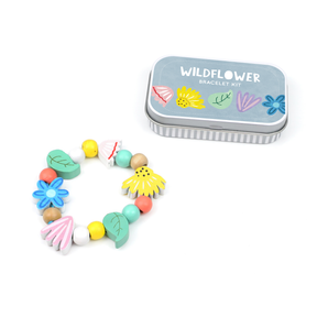 Displayed next to a small metal tin labeled "Wildflower Bracelet Gift Kit," featuring illustrated flowers on the lid, is a colorful beaded bracelet with flower and leaf shapes. The personalized gift tin makes this plastic-free Wildflower Bracelet Gift Kit a charming and eco-friendly present for any occasion.