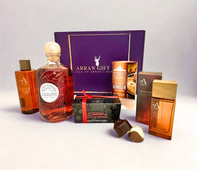 A Deluxe Goatfell Gift Box presented in a purple Arran Sense of Scotland gift box, featuring a bottle of Secret Garden Elderflower & Jasmine Gin, alongside chocolates, soap, shower gel, and ginger rounds—all artfully arranged on a light background.