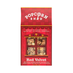 A Red Velvet Gourmet Popcorn Snack Box featuring a vibrant red design and a window that reveals the delicious popcorn inside. The packaging highlights gluten-free, all-natural ingredients, and a unique combination of cream cheese frosting with decadent white chocolate flavor. This irresistible snack is the perfect treat for anyone who enjoys distinctive caramel popcorn creations.