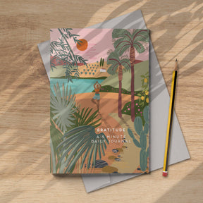 The "Gratitude journal yoga - notebook mindfulness" features a vibrant cover of a person doing yoga by a lake among trees and plants, eco printed and shown beside a pencil and envelope on a wooden surface.