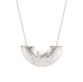 The Caitlin Hegney Gibbous Silver Necklace features a textured, fan-shaped pendant on a delicate chain, showcasing handcrafted artistry against a white background.
