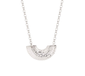 The Caitlin Hegney Gibbous Silver Necklace features a handcrafted, fan-shaped pendant with a ridged, hammered design on a delicate chain, reflecting the artistry of Scottish jewellery against a white background.