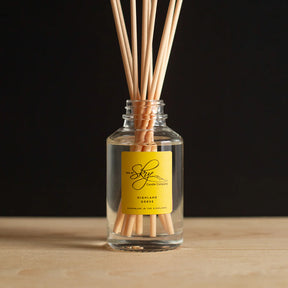A clear glass Highland Gorse Diffuser with reed sticks and gorse fragrance sits on a wooden surface against a black background, labeled "The Skye Candle Company Highland Gorse.