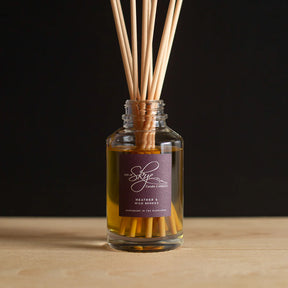 The Heather & Wild Berries Reed Diffuser by Skye Candle Company features a glass jar of yellow liquid with diffuser sticks and blends Scottish heather fragrance with blueberries, blackberries, and raspberries.
