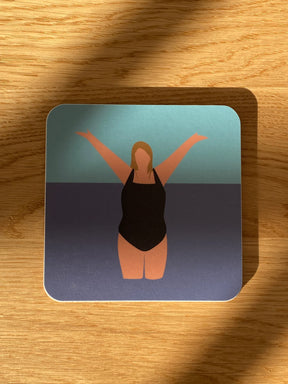 The I Love the Water Coaster showcases a minimalist illustration of a woman in a black swimsuit with arms raised, standing in water against a gradient blue background on a square wooden coaster.