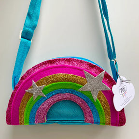 The Children’s Rainbow Bag is a colorful, glittery purse with pink, gold, green, and blue stripes, two silver glitter stars, a turquoise strap, and a white cloud-shaped tag hanging from the strap.