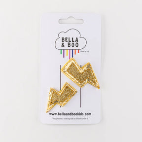 Two gold glitter Lightening Bolt Hair Clips inspired by Harry Potter, attached to a Bella & Boo card with a cloud logo. Metal snap clips are safe and stylish; includes website and choking hazard warning for under 3s.