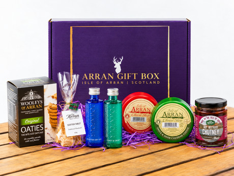 An Original Scottish Gin Lover Gift Box, shown as a purple box containing Downpour miniatures, a box of oatcakes, a bag of tablet, two small bottles of gin, two rounds of cheddar cheese, and a jar of chutney.