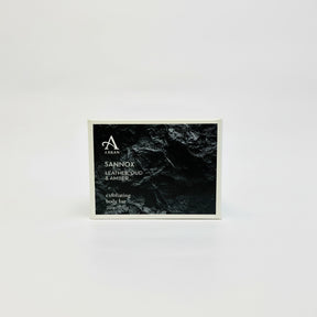 Arran's "Sannox Exfoliating Body Bar Soap 200g" for men comes in striking black packaging. Weighing 200g/7oz, it boasts an invigorating scent of leather, oud, and amber, perfectly showcased against a white background.