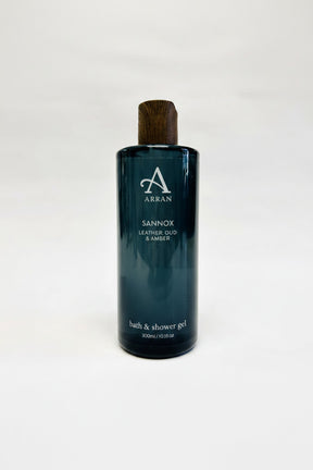 A 300ml (10.1 fl oz) dark green bottle of Sannox Bath and Shower Gel, offering an invigorating "Leather, Oud & Amber" scent. This men's fragrance, complete with a wooden cap, is ideal for a luxurious bathing experience.