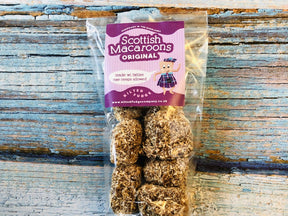 A clear bag of Vanilla Scottish Macaroons, round and handmade, coated in coconut, sits on rustic wood. The label reads “Vanilla Scottish Macaroons,” with a tartan design and website—capturing classic Scottish sweetness.